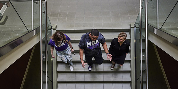 An overhead shot of three students walking down stairs talking to each other.
